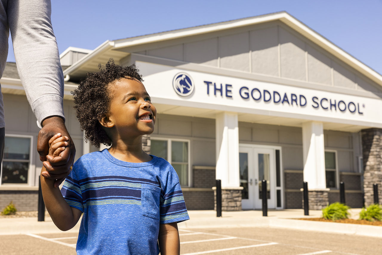 smiling child holding their parent's hand outside of a Goddard School